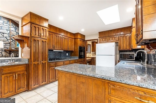 kitchen with a skylight, black appliances, a peninsula, and a sink