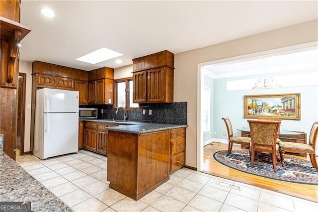 kitchen featuring light tile patterned floors, decorative backsplash, stainless steel microwave, freestanding refrigerator, and a sink