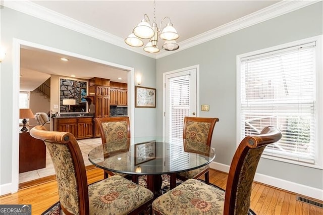 dining room with baseboards, visible vents, an inviting chandelier, crown molding, and light wood-type flooring