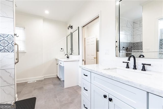 bathroom with a shower, two vanities, a sink, and baseboards