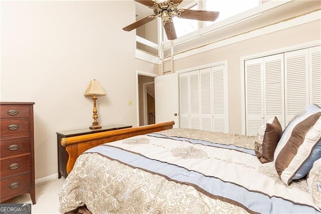 bedroom featuring a high ceiling, a ceiling fan, multiple closets, and light colored carpet