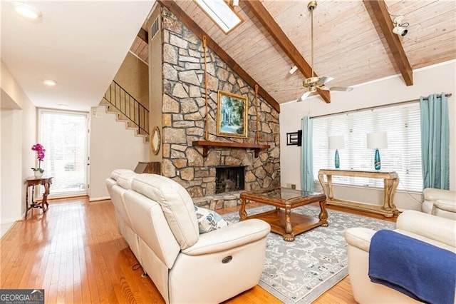 living room with beam ceiling, wooden ceiling, a stone fireplace, and hardwood / wood-style floors