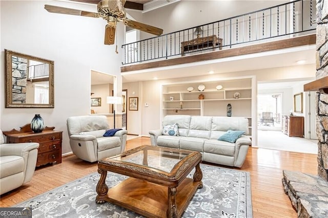 living area featuring built in features, ceiling fan, a towering ceiling, and wood finished floors