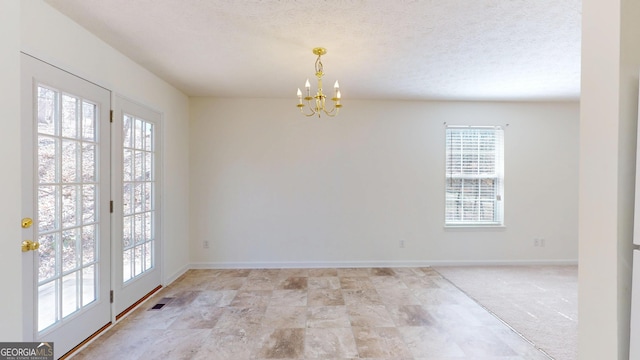 empty room featuring a notable chandelier, plenty of natural light, visible vents, and a textured ceiling