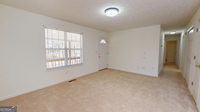 unfurnished room with a textured ceiling, visible vents, and light colored carpet