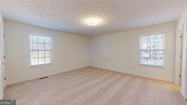 spare room featuring a textured ceiling, visible vents, and light colored carpet