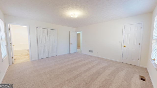 unfurnished bedroom featuring baseboards, visible vents, connected bathroom, carpet, and a textured ceiling