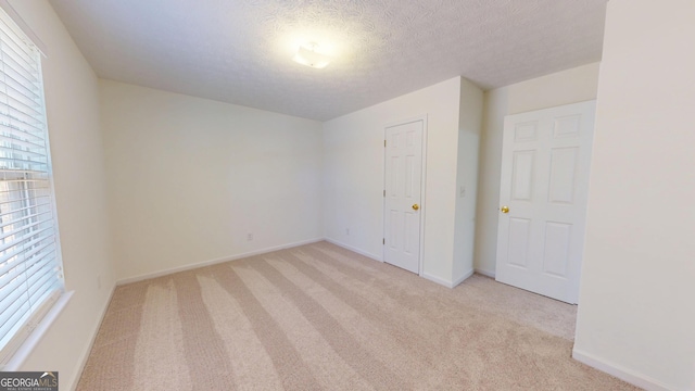 empty room featuring light colored carpet, a textured ceiling, and baseboards