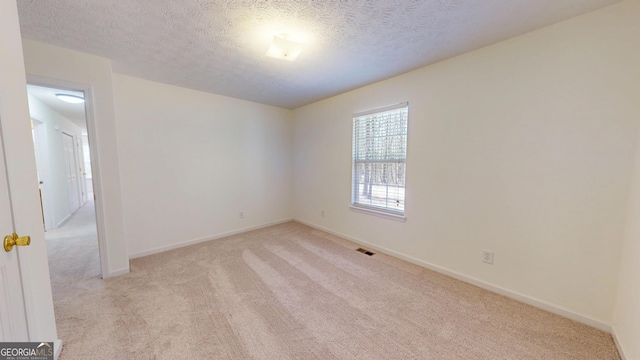 spare room featuring light colored carpet, visible vents, a textured ceiling, and baseboards