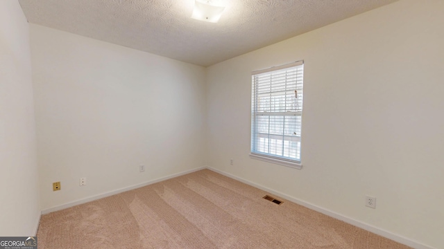 spare room featuring light colored carpet, visible vents, a textured ceiling, and baseboards