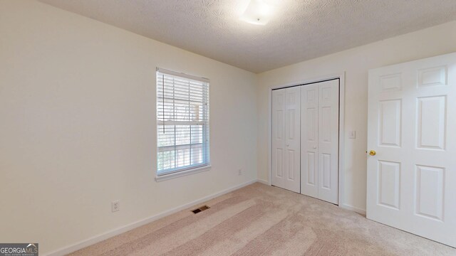 unfurnished bedroom with baseboards, visible vents, light colored carpet, a textured ceiling, and a closet