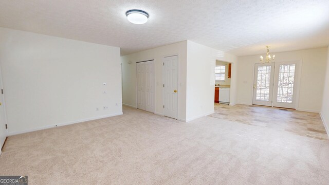 spare room featuring a chandelier, light carpet, a textured ceiling, and baseboards