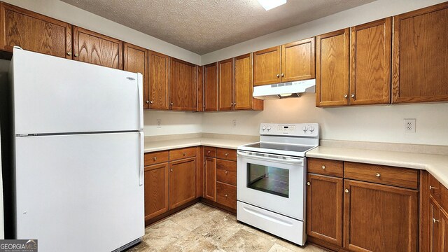 kitchen featuring white appliances, brown cabinets, light countertops, a textured ceiling, and under cabinet range hood