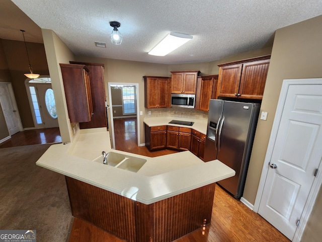 kitchen featuring light countertops, decorative backsplash, appliances with stainless steel finishes, light wood-type flooring, and a peninsula