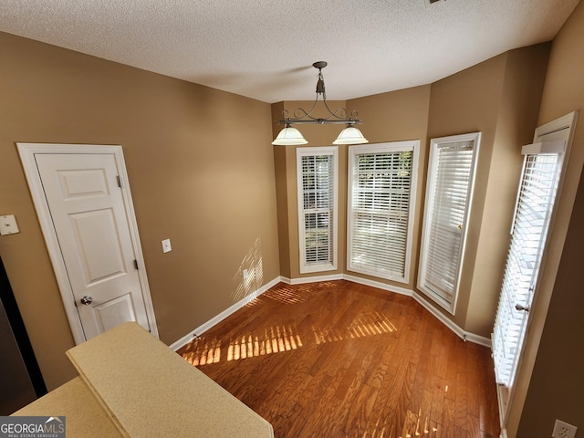 unfurnished dining area with a textured ceiling, wood finished floors, and baseboards