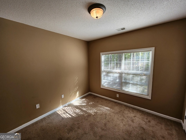 unfurnished room with carpet, a textured ceiling, visible vents, and baseboards