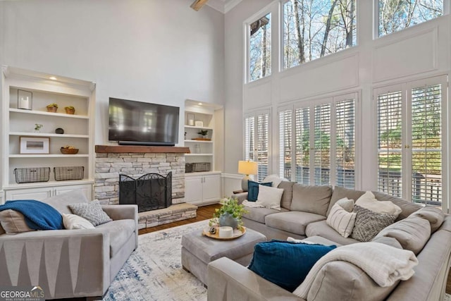 living room with a healthy amount of sunlight, built in features, wood finished floors, and a stone fireplace