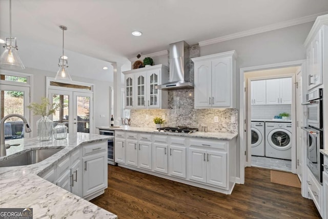 kitchen with wine cooler, appliances with stainless steel finishes, a sink, wall chimney range hood, and separate washer and dryer