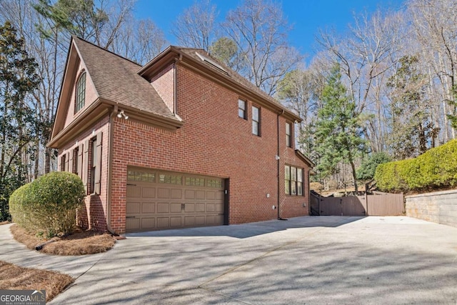 view of side of home featuring a garage, brick siding, driveway, and fence