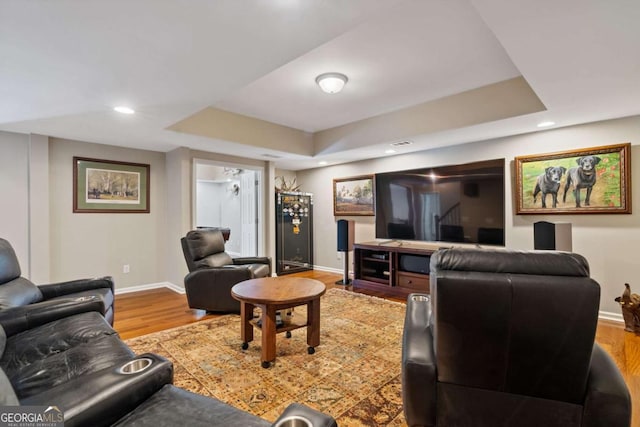 living area with recessed lighting, a raised ceiling, baseboards, and wood finished floors