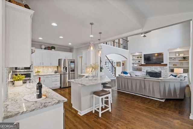 kitchen with a stone fireplace, stainless steel appliances, a peninsula, dark wood-style flooring, and white cabinets