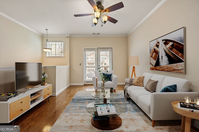 living room featuring baseboards, wood finished floors, visible vents, and crown molding