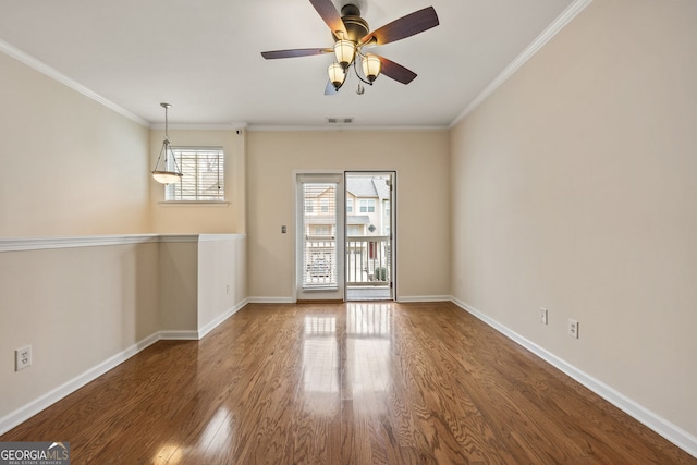 spare room with ornamental molding, visible vents, baseboards, and wood finished floors