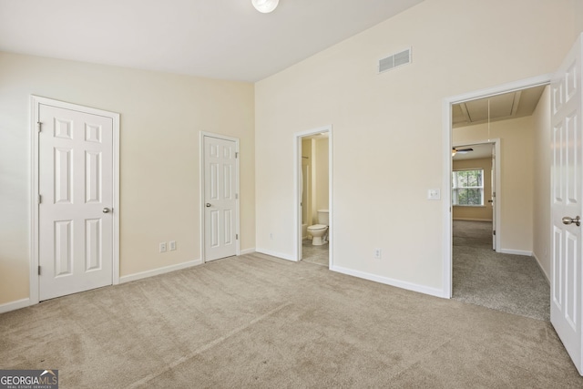 unfurnished bedroom with vaulted ceiling, carpet flooring, visible vents, and attic access