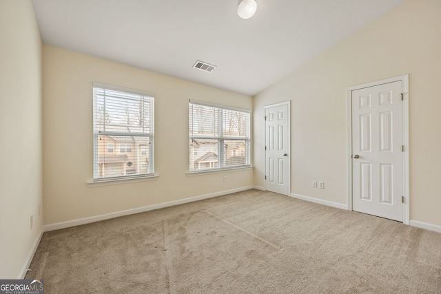 carpeted empty room featuring baseboards, visible vents, and vaulted ceiling