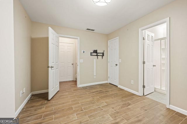 unfurnished bedroom featuring ensuite bath, wood tiled floor, visible vents, and baseboards