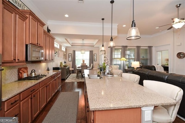 kitchen with dark wood-style floors, appliances with stainless steel finishes, brown cabinets, open floor plan, and a sink