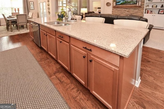 kitchen featuring dark wood-style flooring, a sink, stainless steel dishwasher, and light stone countertops