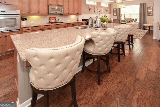 kitchen with dark wood-style floors, decorative backsplash, white microwave, a sink, and oven