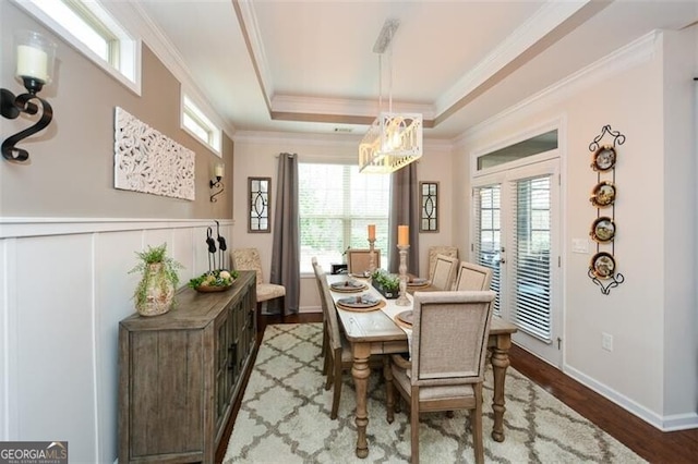 dining room with a wainscoted wall, a tray ceiling, wood finished floors, and ornamental molding