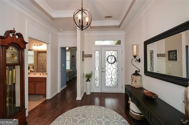 entrance foyer with visible vents, a raised ceiling, dark wood-style floors, ornamental molding, and an inviting chandelier