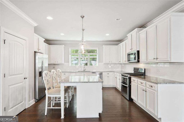 kitchen featuring stainless steel appliances, a kitchen island, a sink, white cabinets, and a kitchen bar