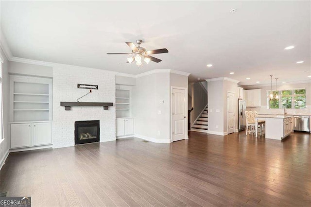 unfurnished living room with dark wood-style flooring, a fireplace, ornamental molding, baseboards, and stairs