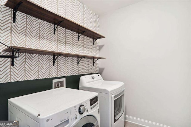 clothes washing area featuring an accent wall, laundry area, baseboards, and washer and clothes dryer