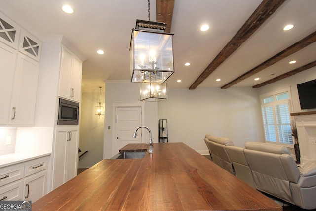 kitchen with beam ceiling, stainless steel microwave, open floor plan, a sink, and butcher block countertops