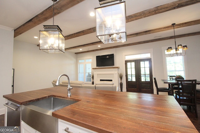 kitchen with butcher block counters, a sink, white cabinetry, beamed ceiling, and an inviting chandelier