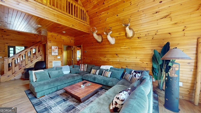 living room with wooden walls, visible vents, a towering ceiling, wood finished floors, and stairs