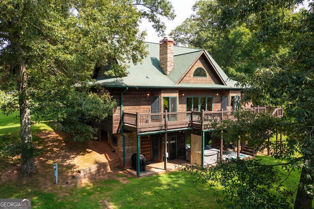 rear view of house featuring a chimney, a deck, a lawn, and a patio