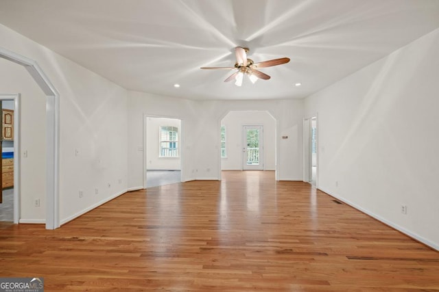 unfurnished living room featuring arched walkways, recessed lighting, light wood-style floors, ceiling fan, and baseboards