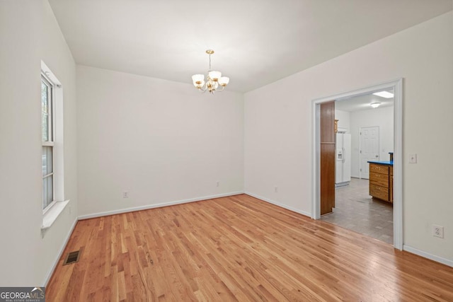 unfurnished room with baseboards, light wood-style flooring, visible vents, and a notable chandelier