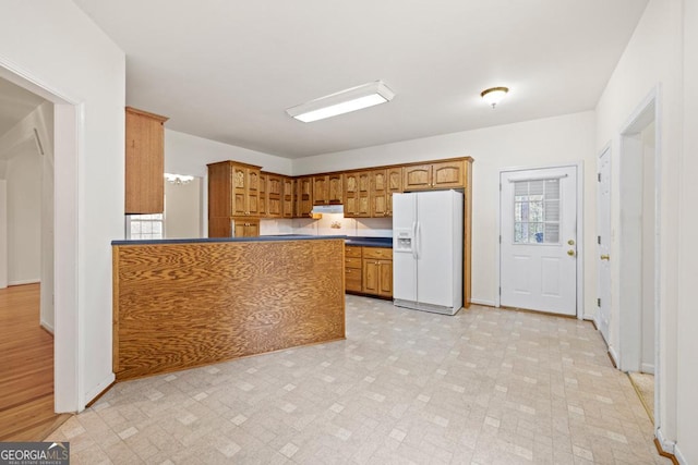 kitchen featuring baseboards, brown cabinets, a peninsula, light floors, and white fridge with ice dispenser