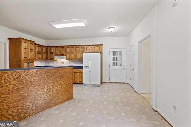 kitchen featuring white refrigerator with ice dispenser, baseboards, dark countertops, brown cabinets, and light floors