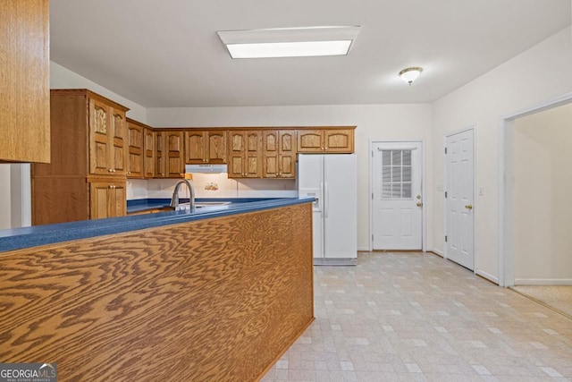 kitchen with under cabinet range hood, white refrigerator with ice dispenser, a sink, brown cabinets, and dark countertops