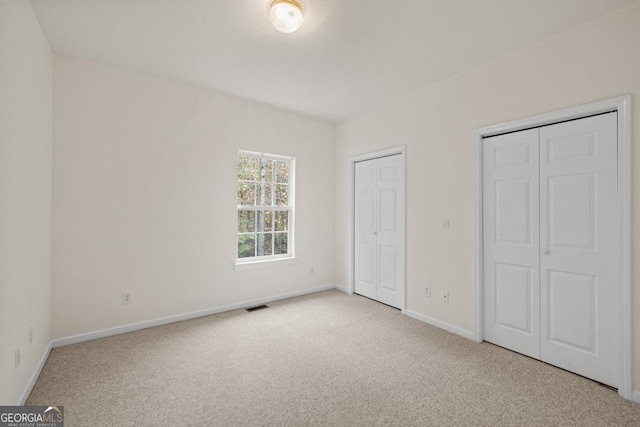 unfurnished bedroom featuring visible vents, baseboards, carpet, and two closets