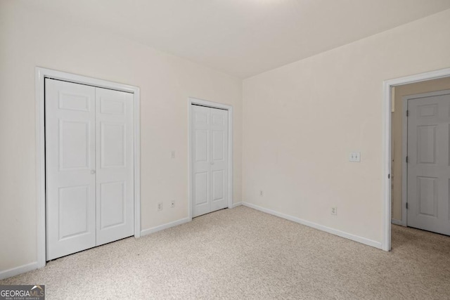 unfurnished bedroom featuring carpet floors, baseboards, and two closets