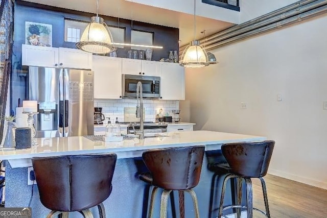 kitchen with a breakfast bar area, decorative backsplash, stainless steel appliances, hanging light fixtures, and white cabinetry